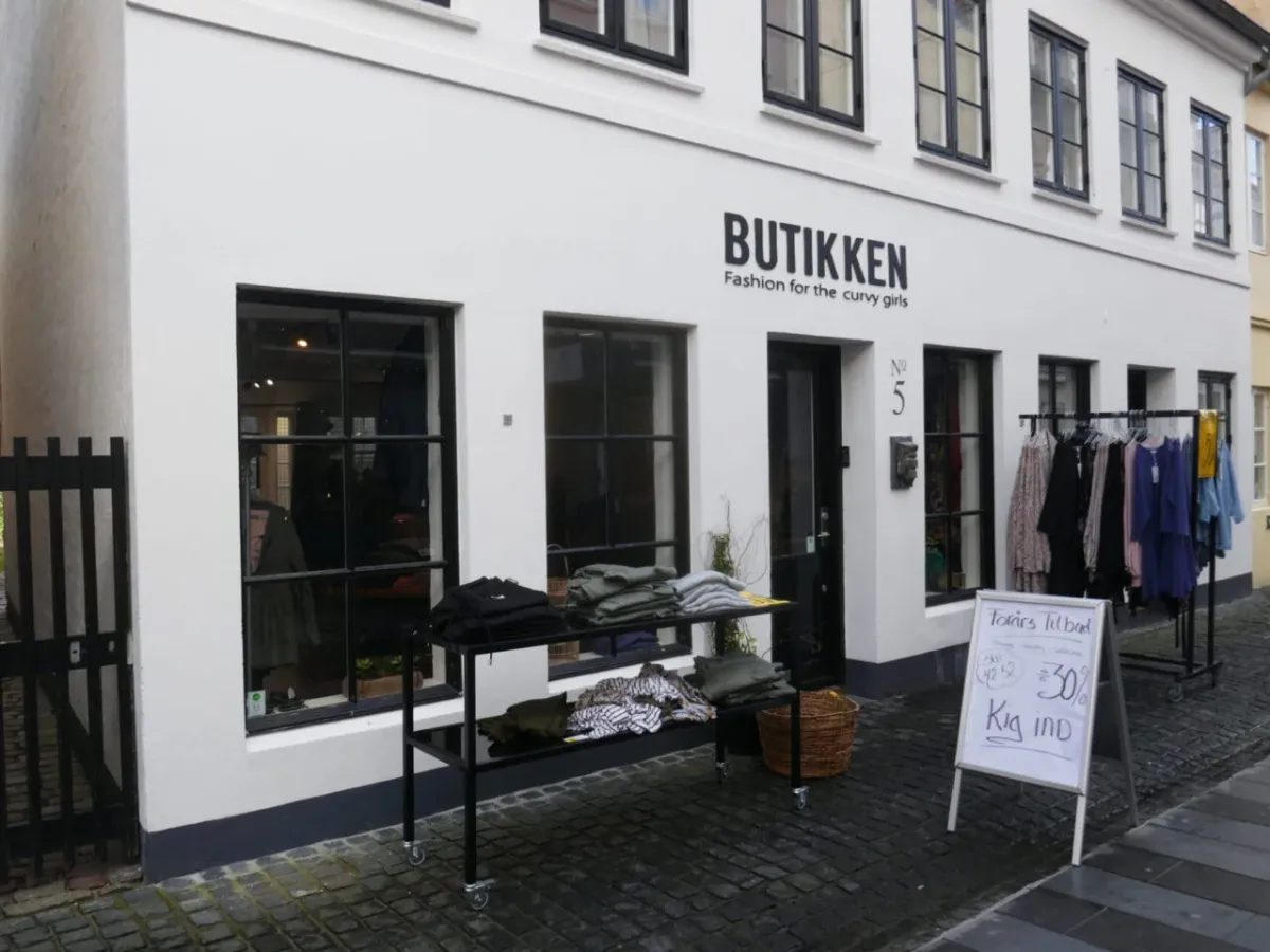 Butik Butikkken med mode til kurvede kvinder, og en sort vogn med tøj og en hængeklædeskab udenfor.