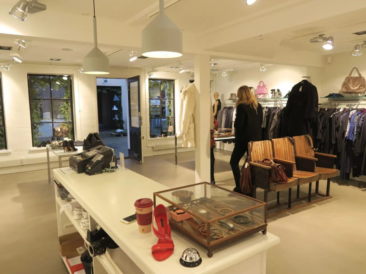 Moderne butik med lyse loftslamper, træstole og lædertasker på hylder og tøjstativet