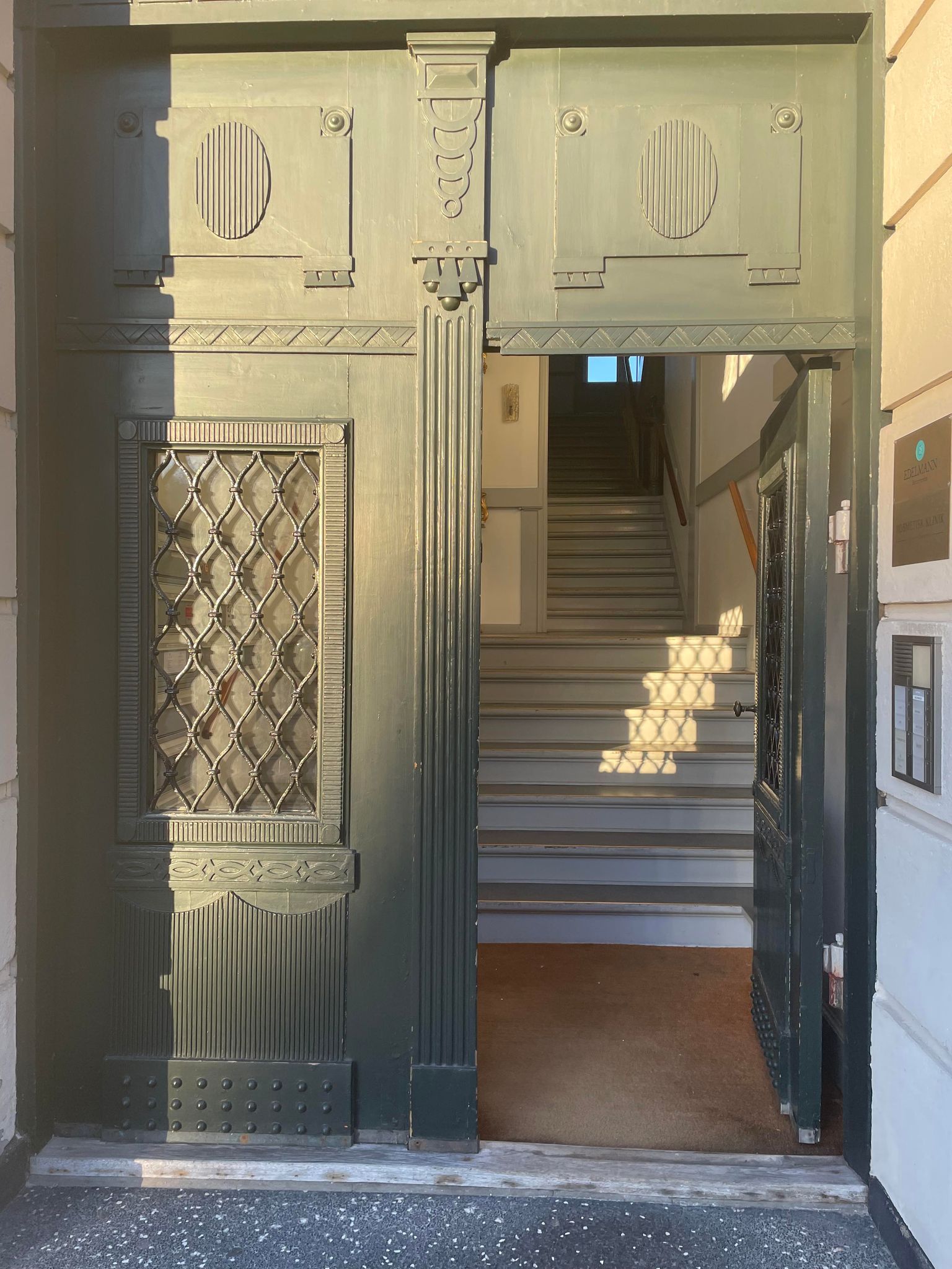 Indgangsdør til bygning med grønne døre og glasindsats, åben dør med trappe og lyserefleks.