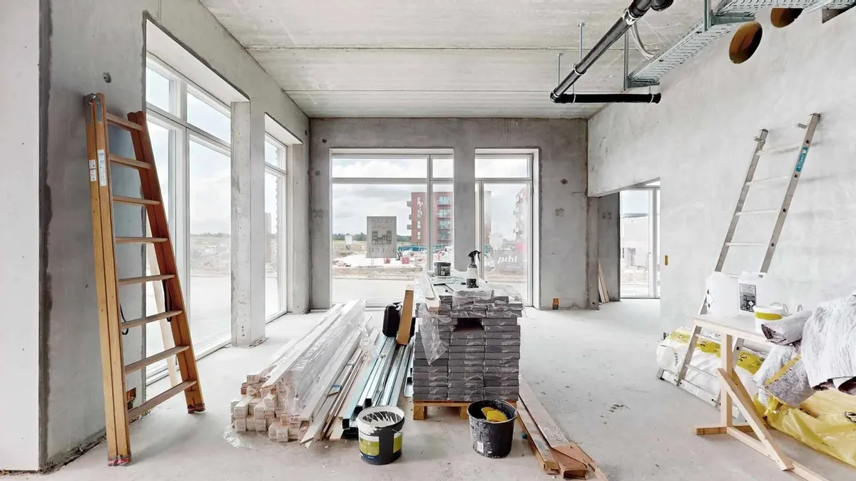 I et stort rum står to træstiger. Der er også to tønder og en pakke med plastfolie. Der er også en høj pakke med plastfolie