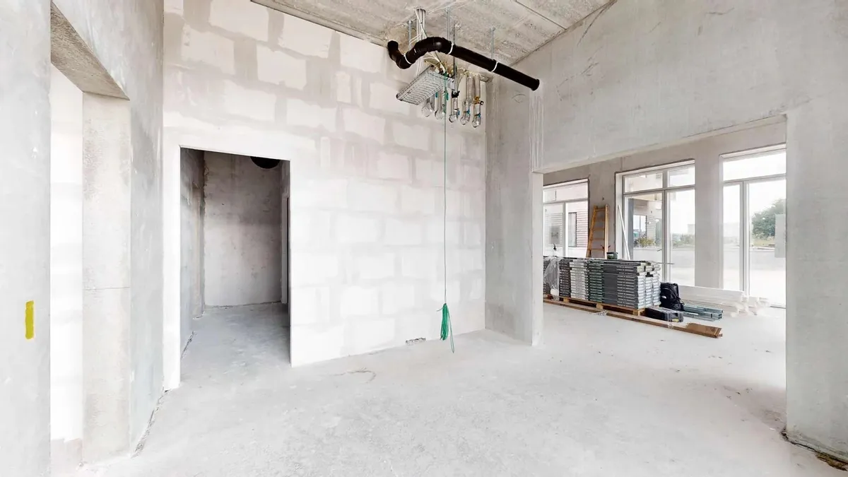 En ny bygning med hvide vægge og gulve, et loft med en hængende lampe og rør samt en række materialer og værktøj i rummet