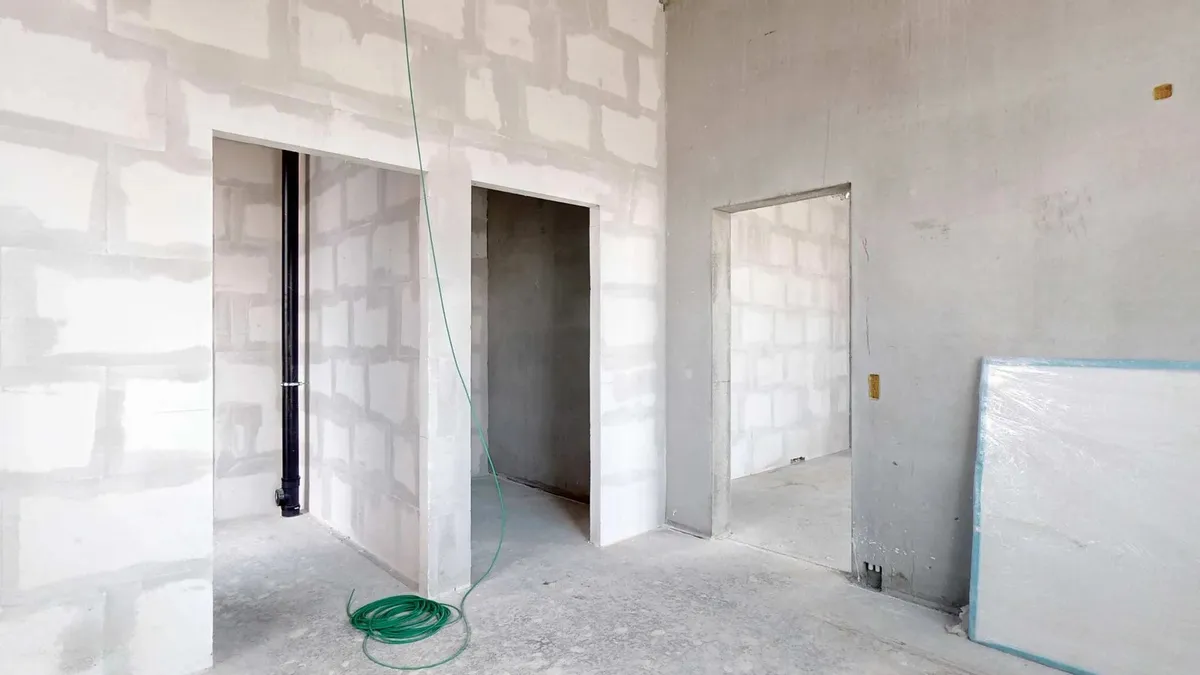 En nybygget lejlighed med hvide vægge og åbninger til døre og vinduer samt en grøn slange og en hvid plakat på siden