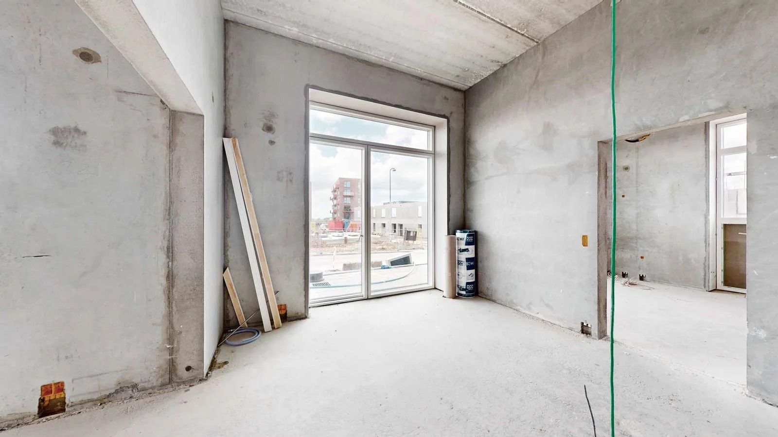 En stor, tom rum med hvide vægge og gulv samt store glasvinduer og åbninger til næste værelse