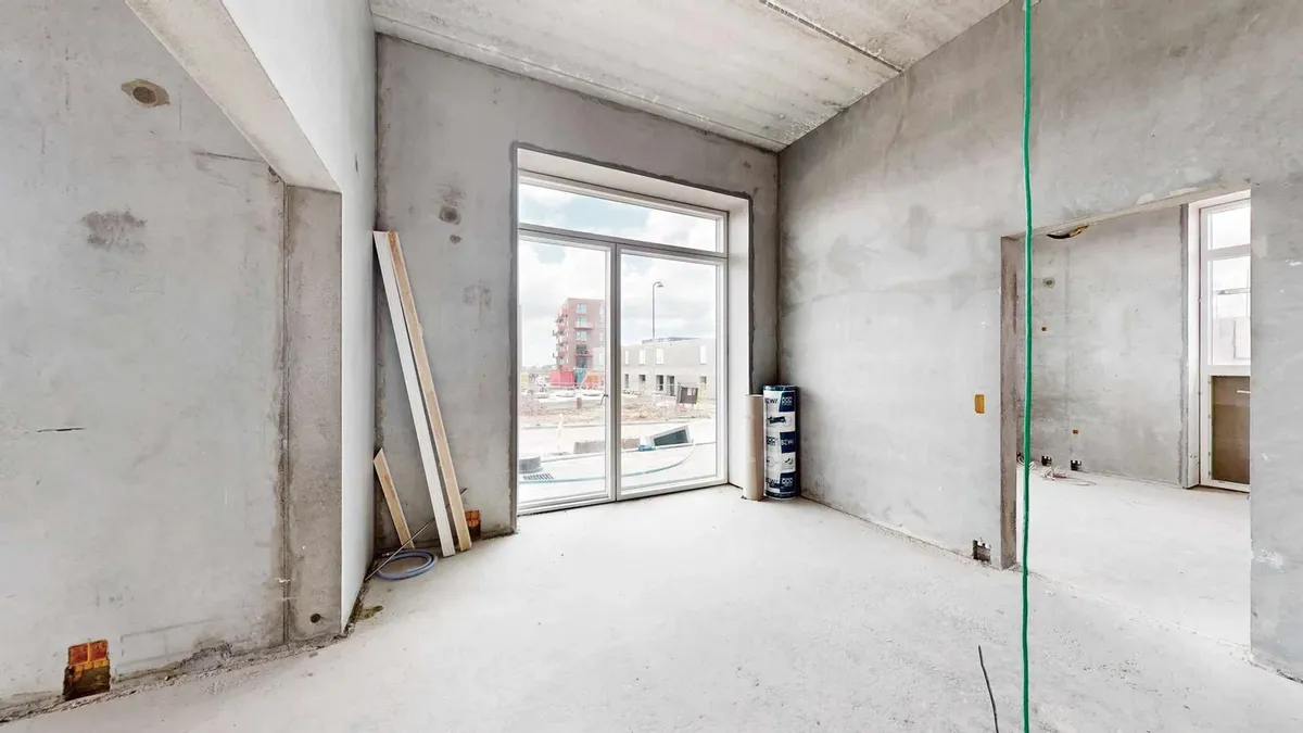 En stor, tom rum med hvide vægge og gulv samt store glasvinduer og åbninger til næste værelse