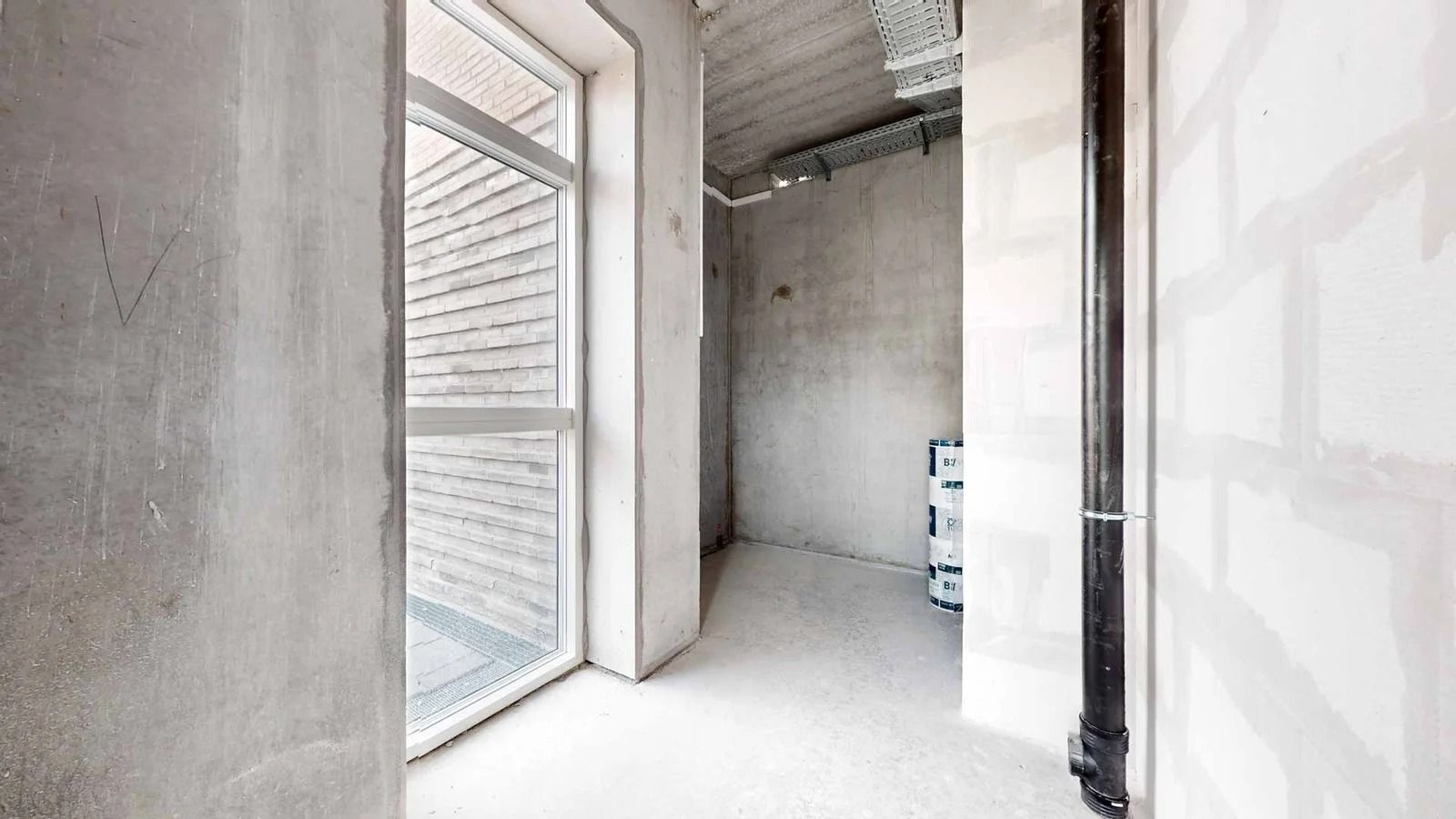 Kort indgangsområde med højt loft og vinduer mod en stenmur i baggrunden og et enkelt vindue mod en anden mur