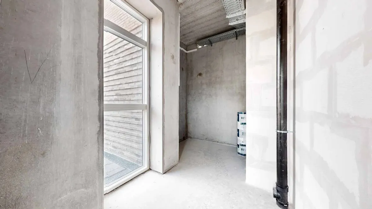 Kort indgangsområde med højt loft og vinduer mod en stenmur i baggrunden og et enkelt vindue mod en anden mur