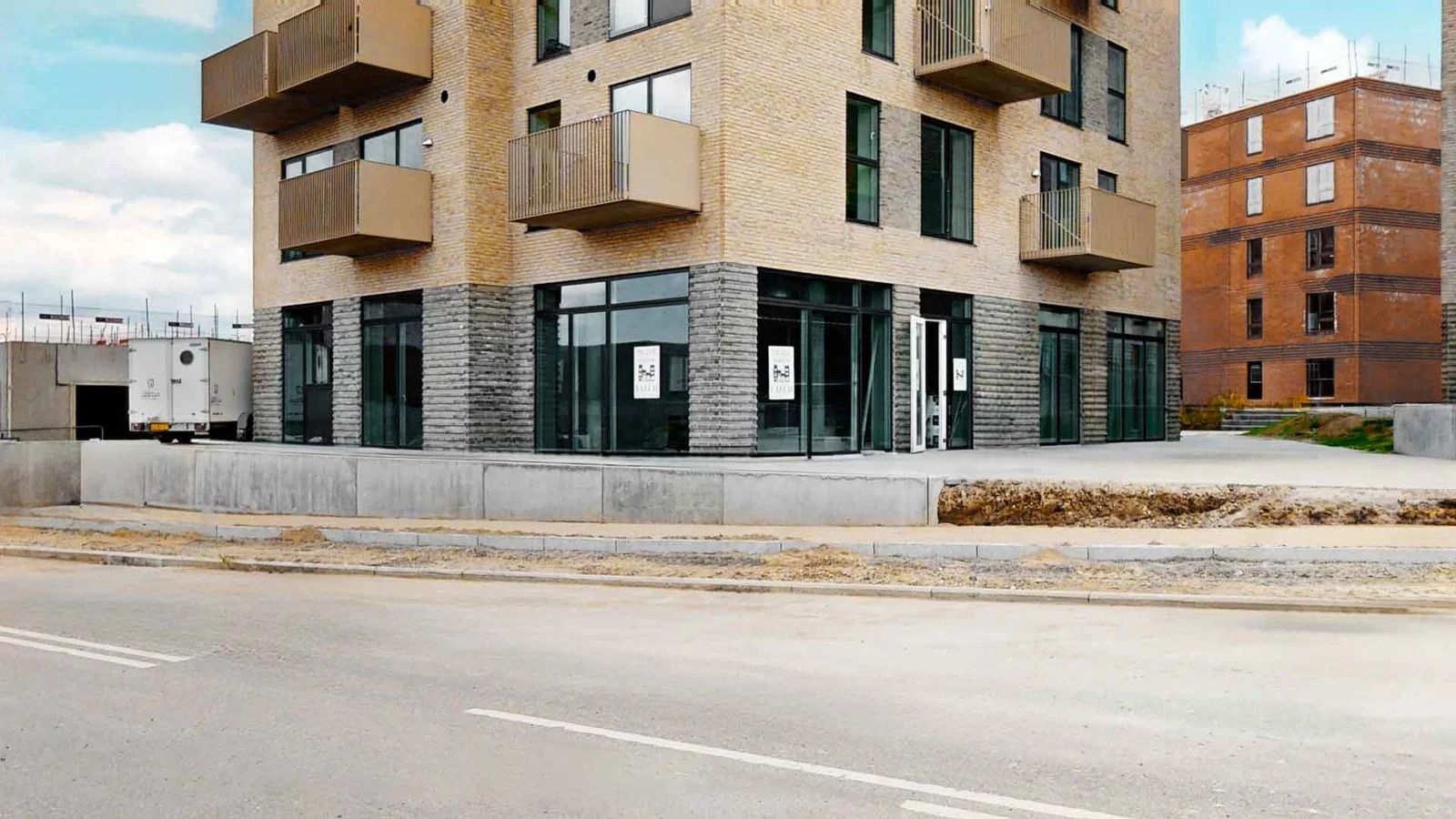 Et nybygget lejlighedskompleks med moderne udformning og mange terrasser samt en hvid trailer parkeret foran en nybygget