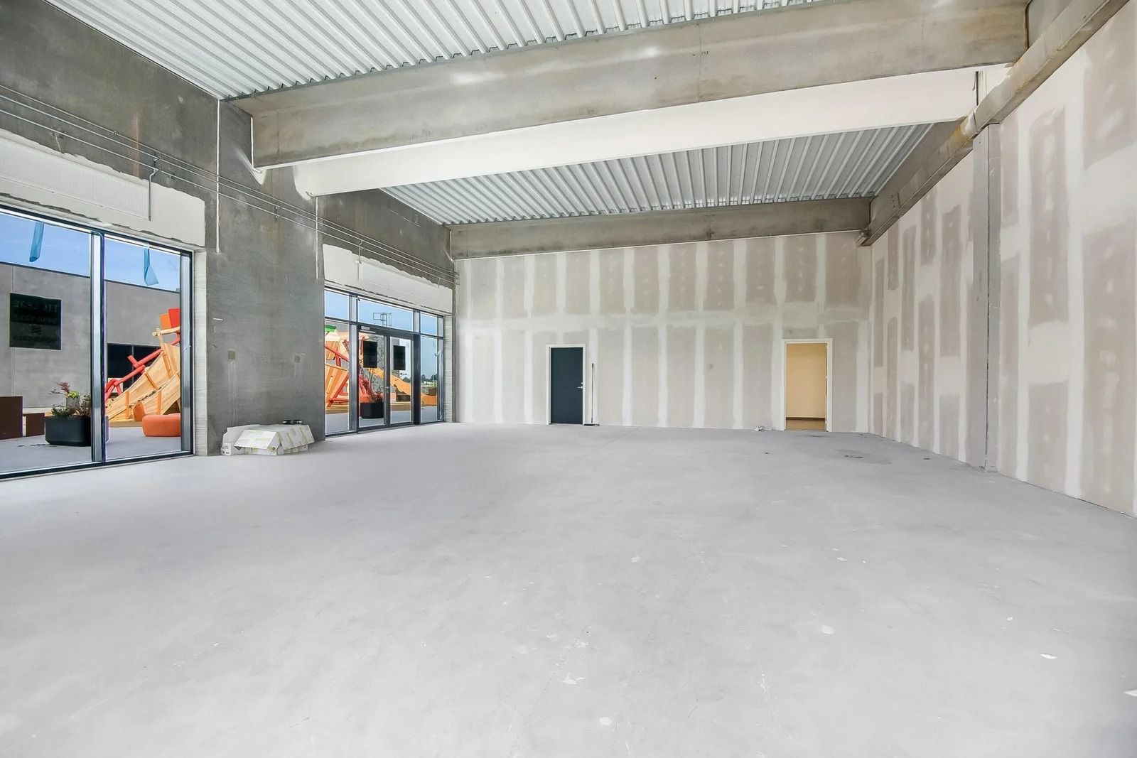 En stor, tom og lyserummelig værkstedslokal med glasdøre og store vinduer mod den ene side og en hvid og grå indre væg