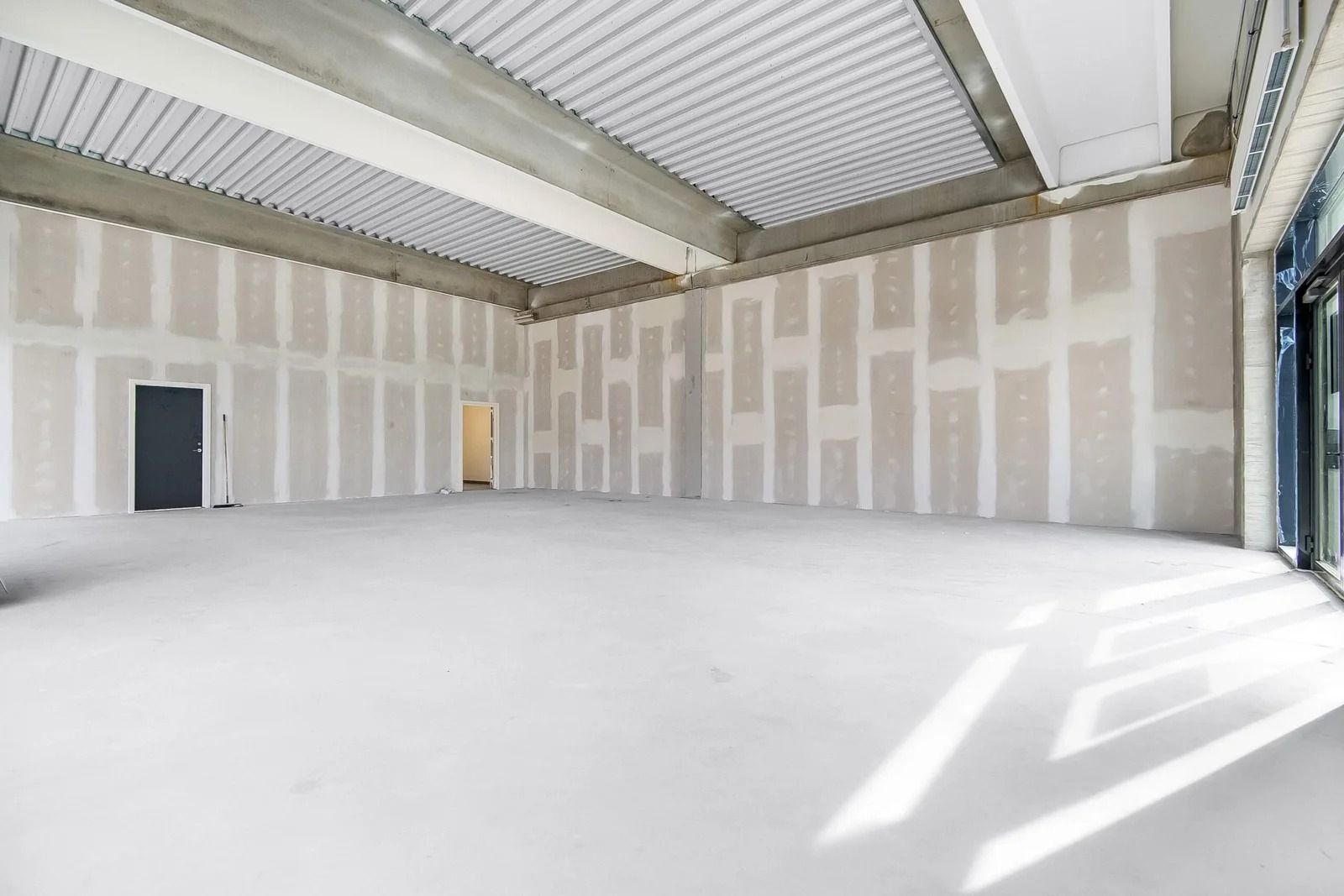 Stort tomt lokale med hvide vægge og loft, hvor der er anlagt vægbeklædning, og der er et glasdøre og et dørblad i den ene