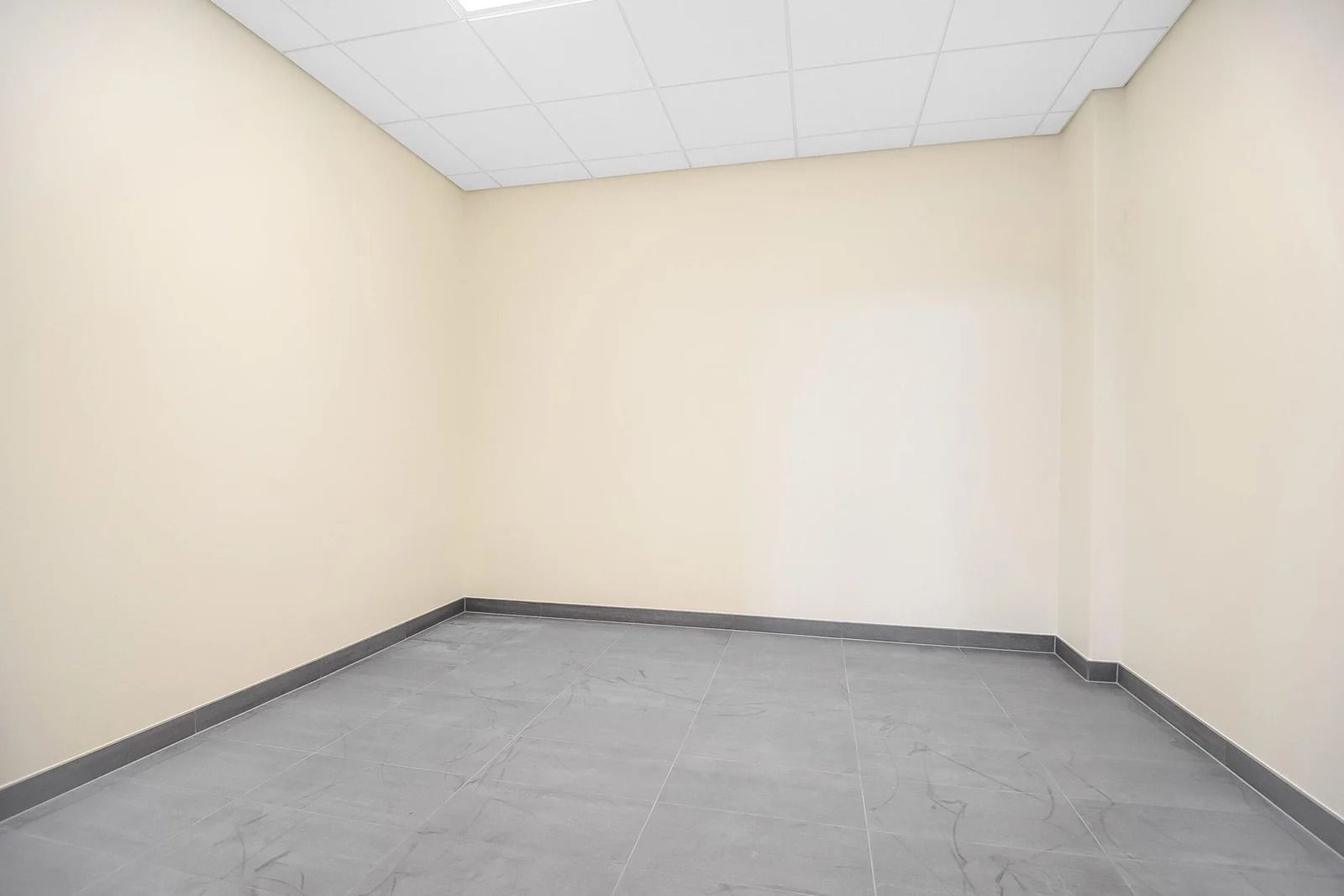 En tom og ren rum med lyse beige vægge og lysegrå gulvfliser med mørkekanter og hvidt loft