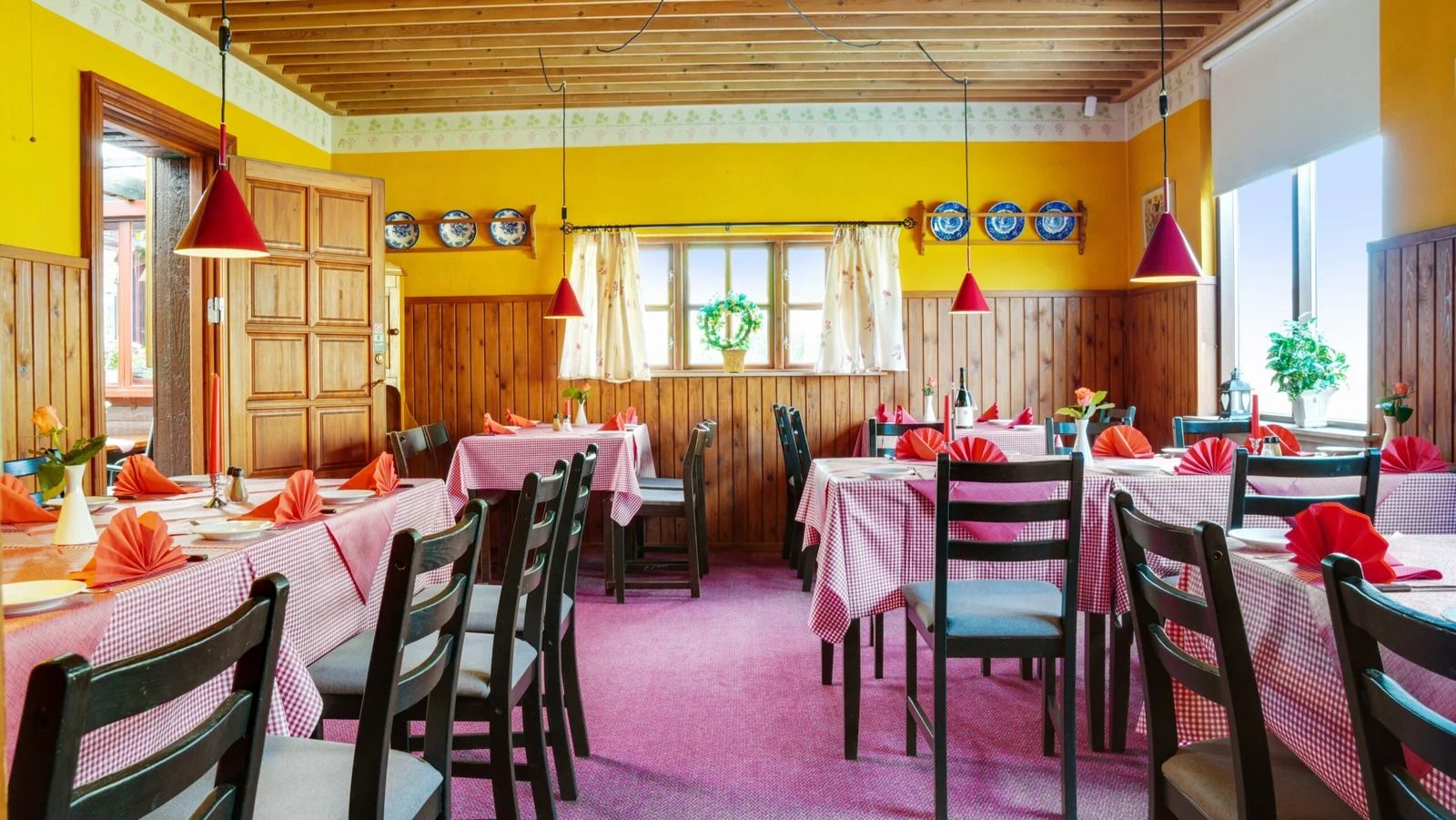 Lyserød og hvid indretning i restaurant med grønne planter og røde paraplyer på bordene