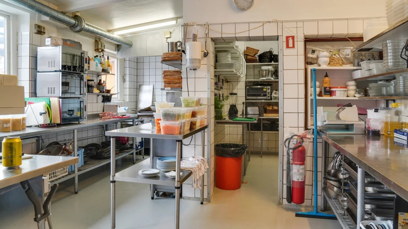 En stor, ren og moderne køkkenafdeling med høje, smukke vægge, flere bordplader, en rødt affaldskur, en brandekstinger og en