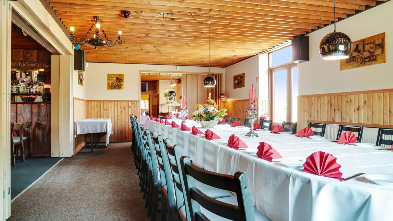 En stor festsal med lange borde, der er dækket med hvide kluder og røde servietter og en lysekronehængende loft.