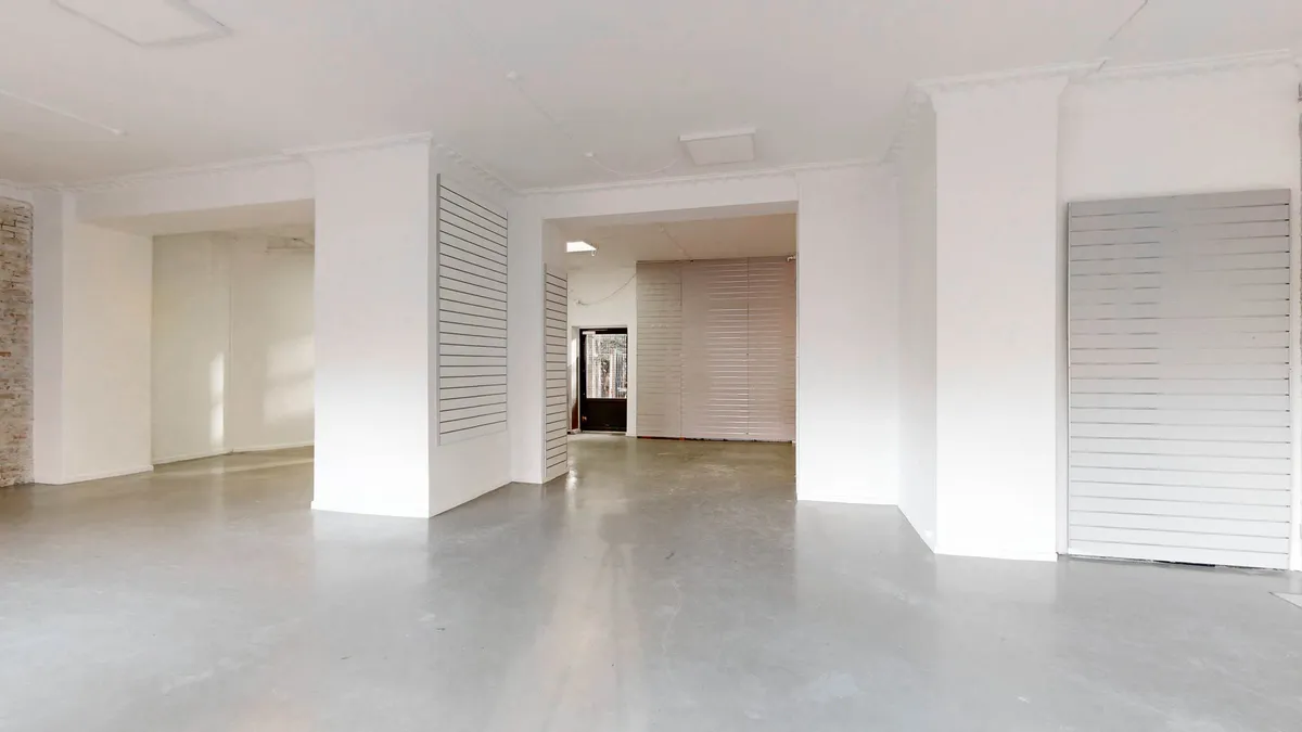 En tom, hvid malet og nyrenoveret erhvervslejlighed med lysegult gulv og lysegrå vægge. Lejligheden har store åbninger og