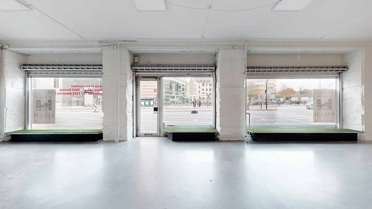 Tomt lokale med glasvinduer og lysegule vægge. Store vinduer med skrift, der hedder "Hoiai". To senge med græsmåtter og