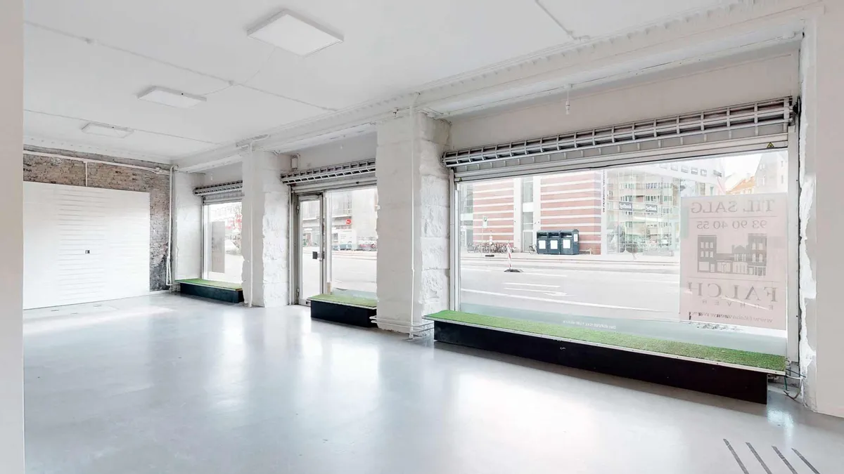 Lys kontorlokaler med store vinduer og en grønt kantede sofa langs den ene side