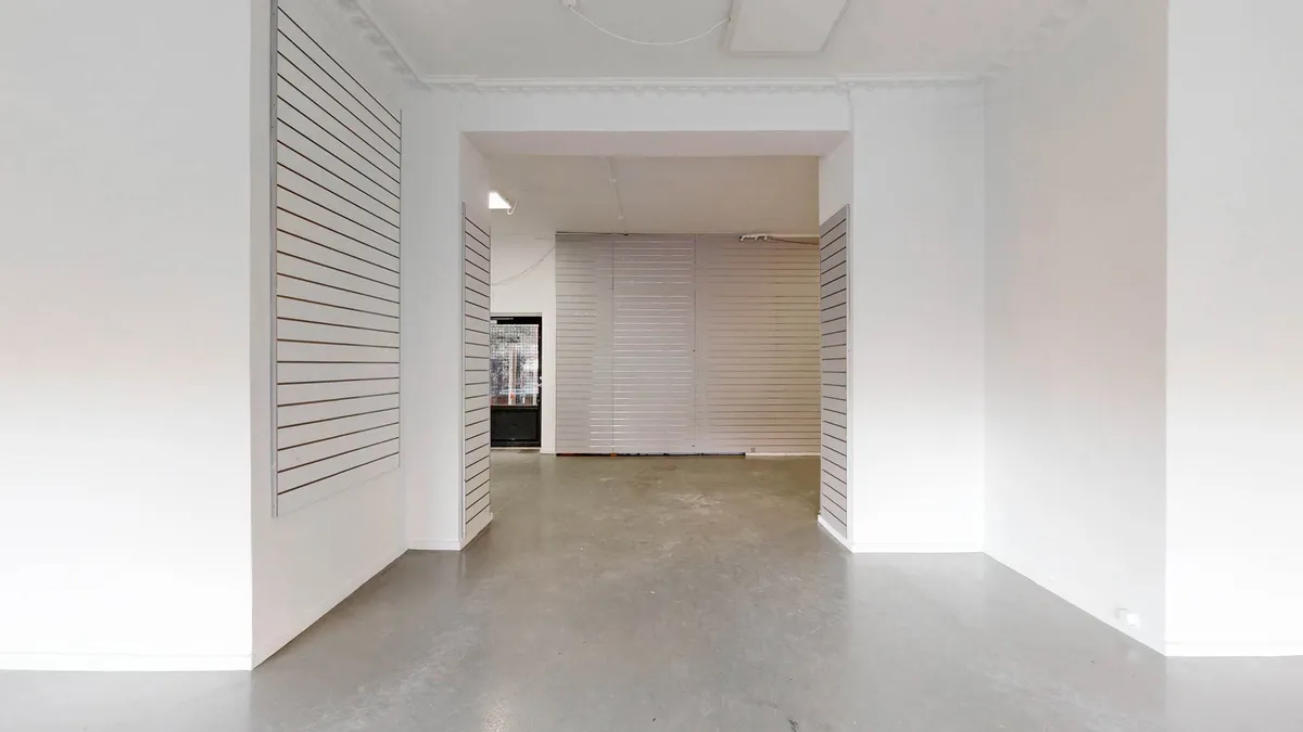 Hvidmalet erhvervslejlighed med gulv, hvide vægge og loft. Store hvide ruder og to hvide skraldespande udenfor.