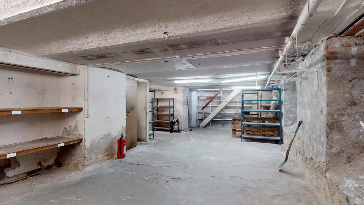 En tom kælder med vægge og loft af beton og træhylder samt en brandhætte og en stige