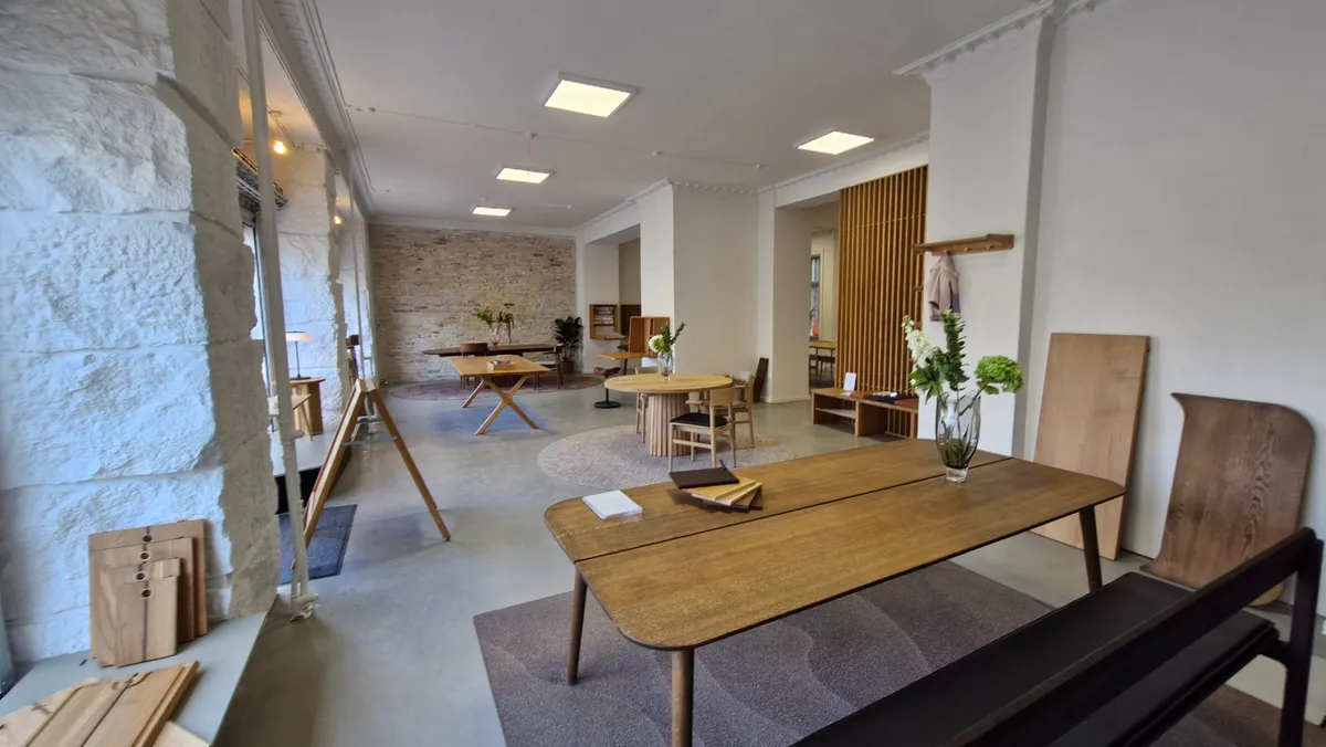 Moderne kontorlokaler med lyse møbler og plante- og blomsterdekorationer. Et stort træbord med to høje og et skrivebord.