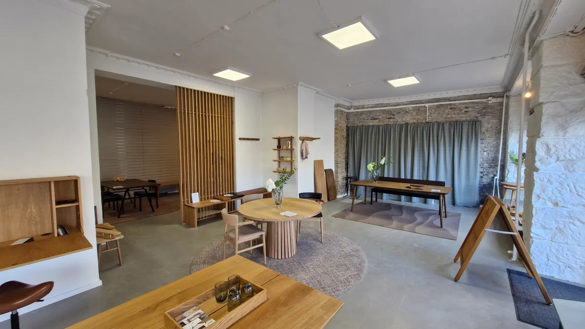 Modernt og minimalistisk indrettet lokale med massivt træ og lyse loftslamper, runde og firkantede borde, og stole samt