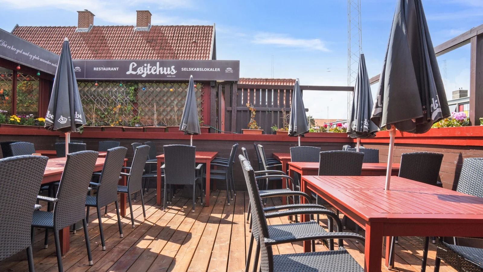 Terrassen med trægulve og røde borde, hvor der er flere stole og parasoller, er en del af restauranten Lajtehus i Kastrup