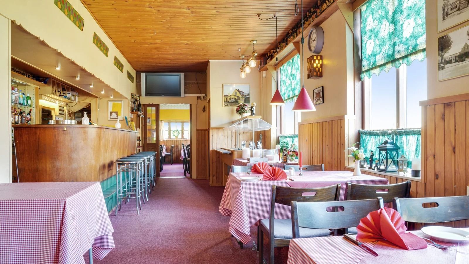 Restaurant med masser af borde og stole og en bar med alkohol og glas.