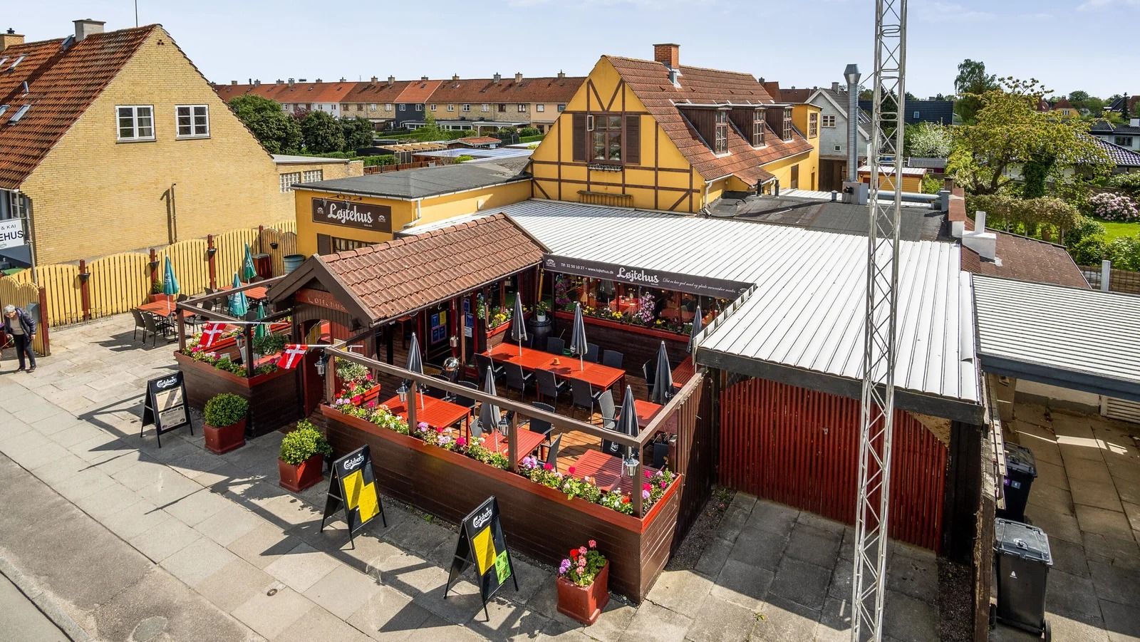 Løjtehus restaurant med terrasse, plantepots og røde borde og stole samt træstokke og parasoller