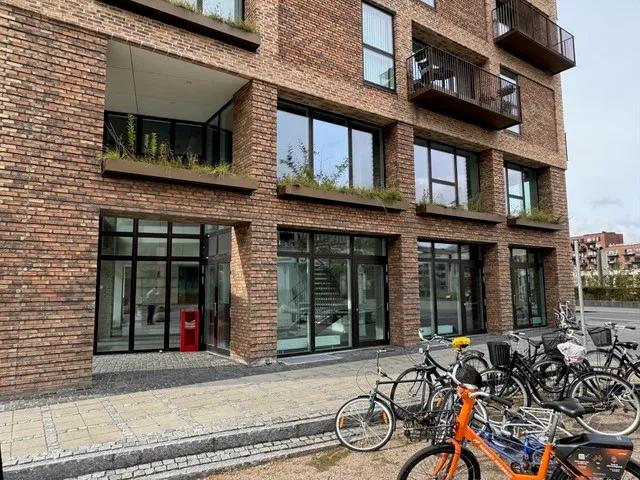 En stor bygning med røde mursten og terrasser med plantepoteter udenfor og cykler parkeret på fortovet