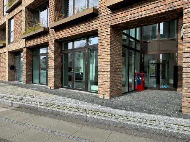 Et nybyggeri med glasvinduer og røde postkasser på gaden, sammen med røde huse i baggrunden