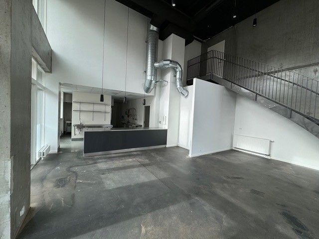 En stor åben stue med højloft, lyse gulve og loftsvinkler. Stalen og hvide vægge med lyse loftslampe og stige til øverste