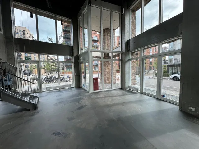 I det åbne, rummelige lokale ser vi lyse vinduer og store glasdøre. Der er en bred trappe og et rødt affaldskur, som er