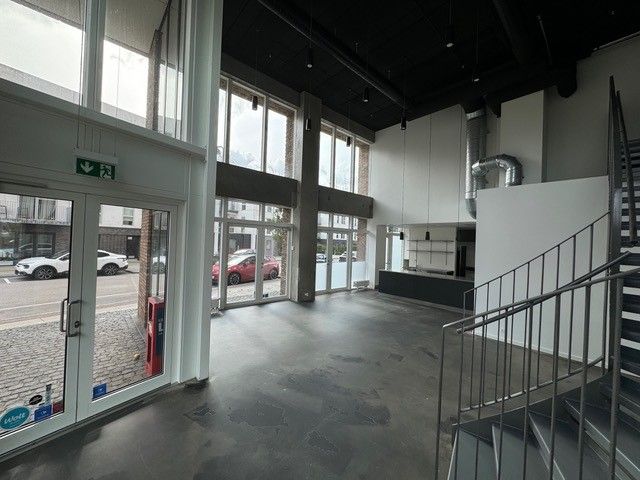 En tom bygning med glasdøre og vinduer med røde biler parkeret udenfor og stige til anden etage