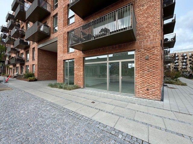 Bygning med terrasser og glasvinduer og glasdøre med søjler uden for terrasserne. En paviment og grønne planter foran