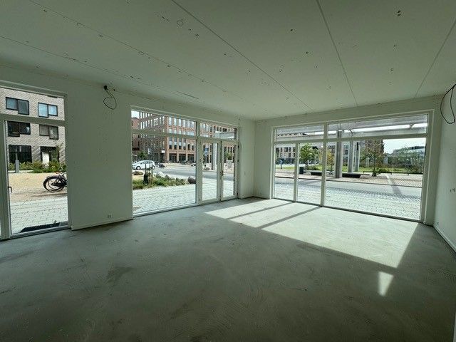 En tom og renoveret butik med store ruder og glasdøre mod en bred gade med biler og planter