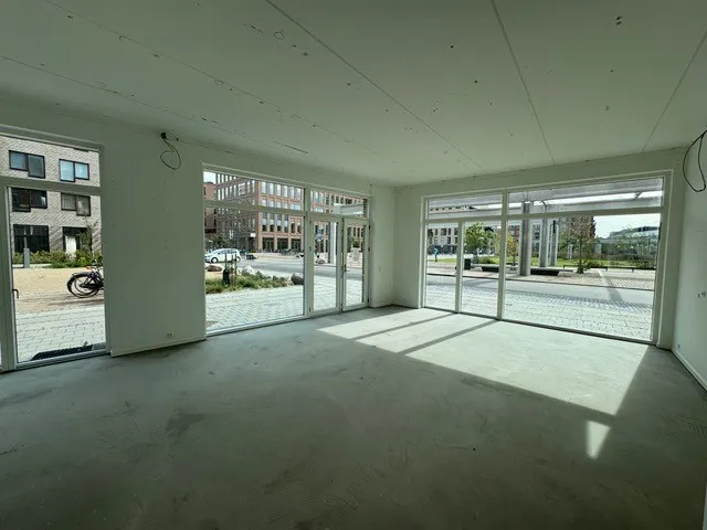 En tom og renoveret butik med store ruder og glasdøre mod en bred gade med biler og planter