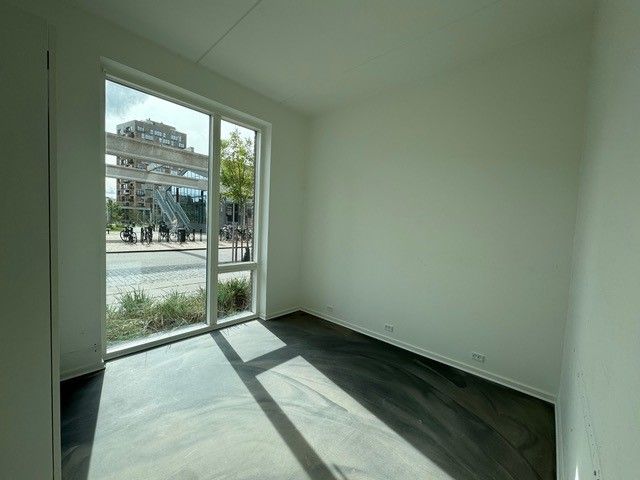 Tom rum med hvide vægge og gulve, glasdøre og vinduer og udsigt til byggede huse og grønne områder