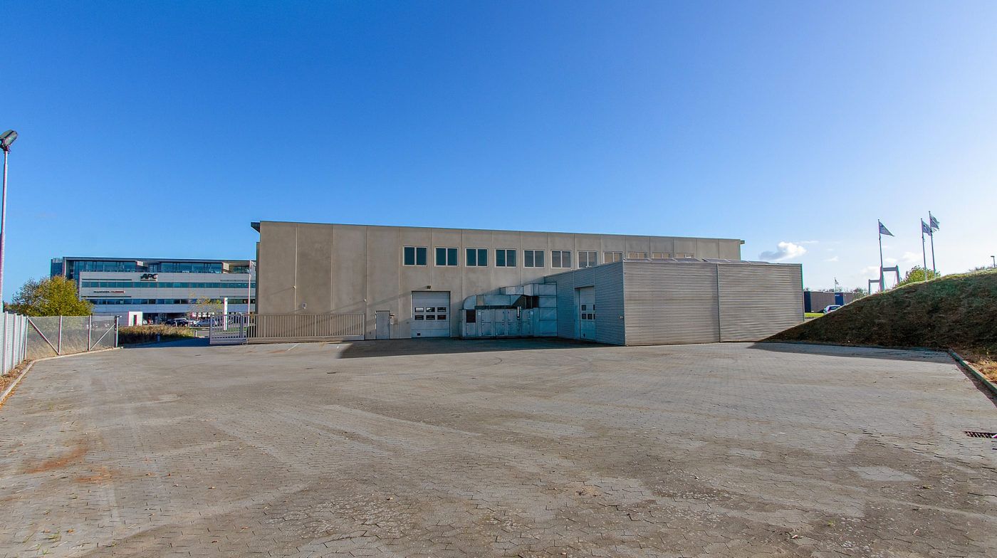 Et stort lager med garagedøre og flere indgange og vinduer på øverste etage og flere flag på toppen af bakken