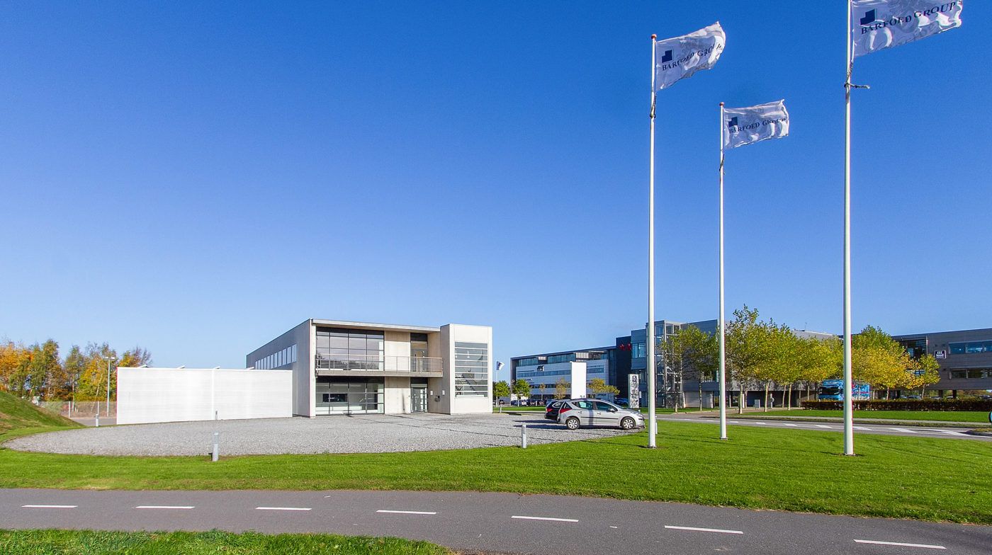 Lejlighedsbygning med flag på høje stænger og to biler parkeret foran.