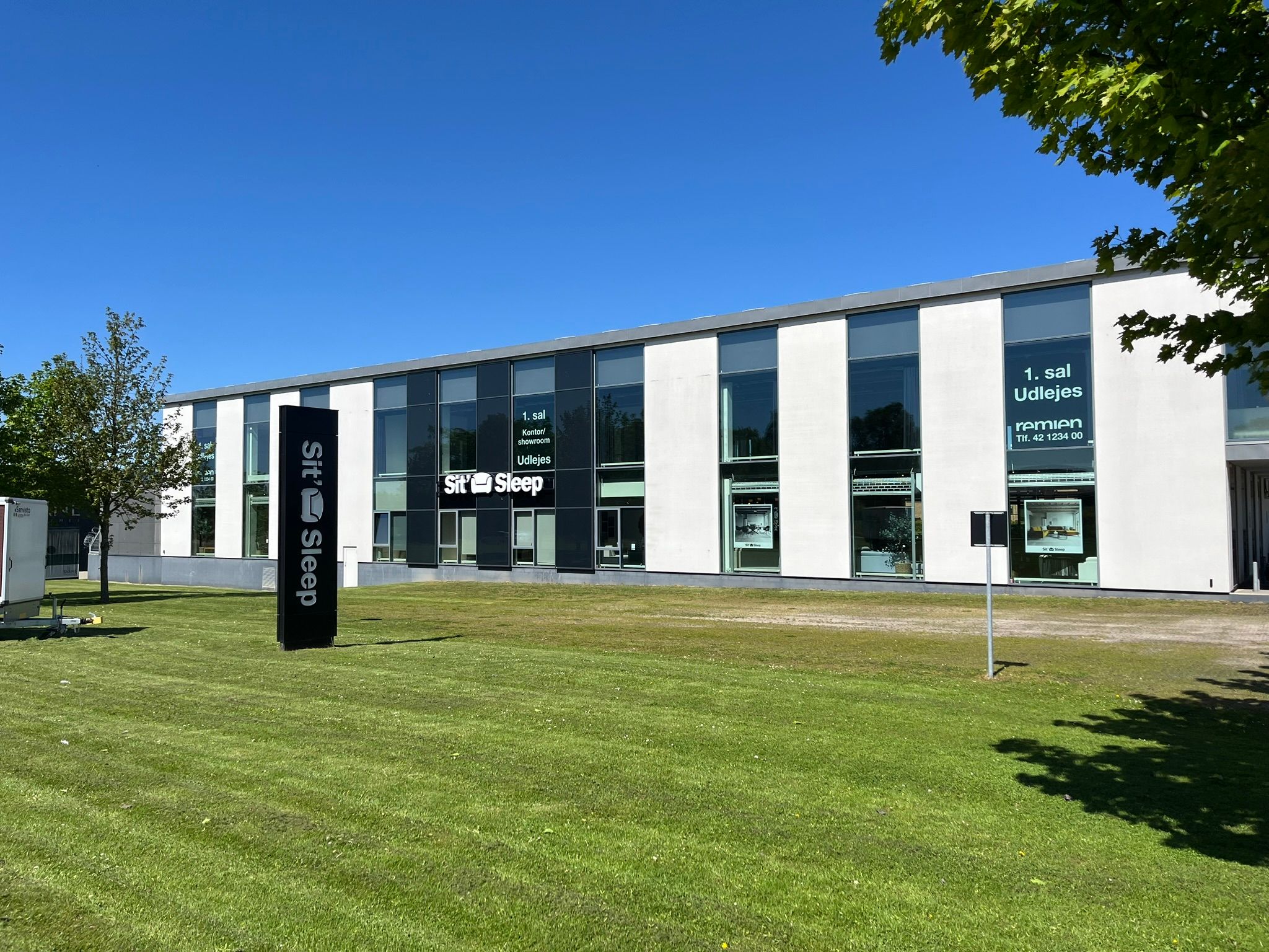 Store, hvide bygninger med glasruder og møbelforretning Sit og Sleep. Alle bygninger har reklameskilt og smukke