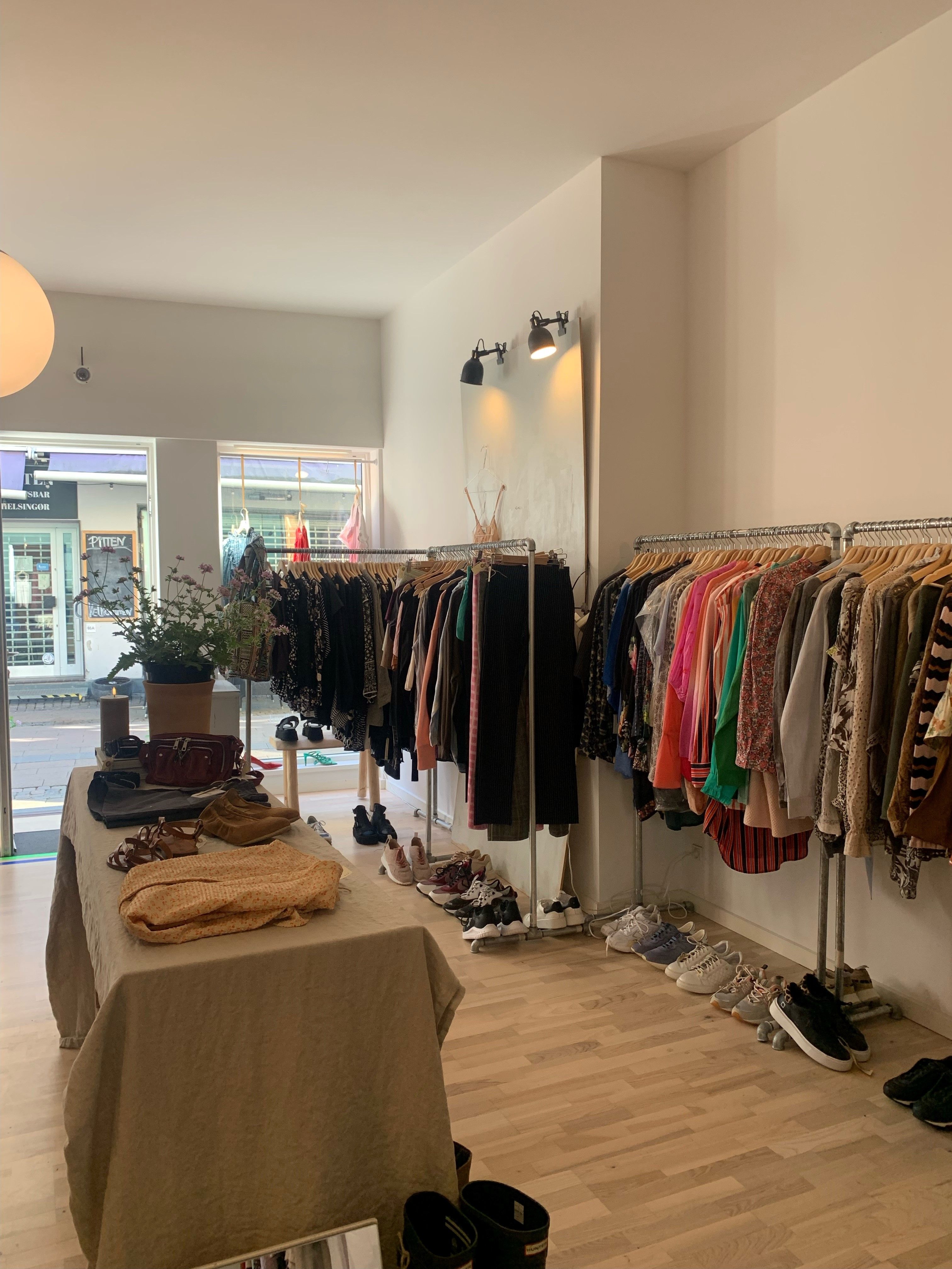 Butik med mange forskellige tøj samt sko og tasker. De fleste tøj er hængt på tøjstænger og tøjregaller, mens sko og tasker