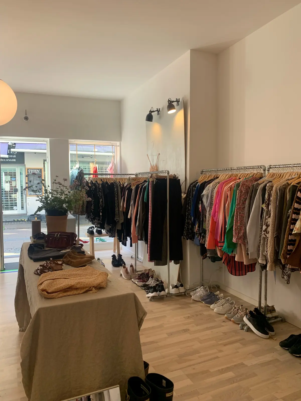 Butik med mange forskellige tøj samt sko og tasker. De fleste tøj er hængt på tøjstænger og tøjregaller, mens sko og tasker