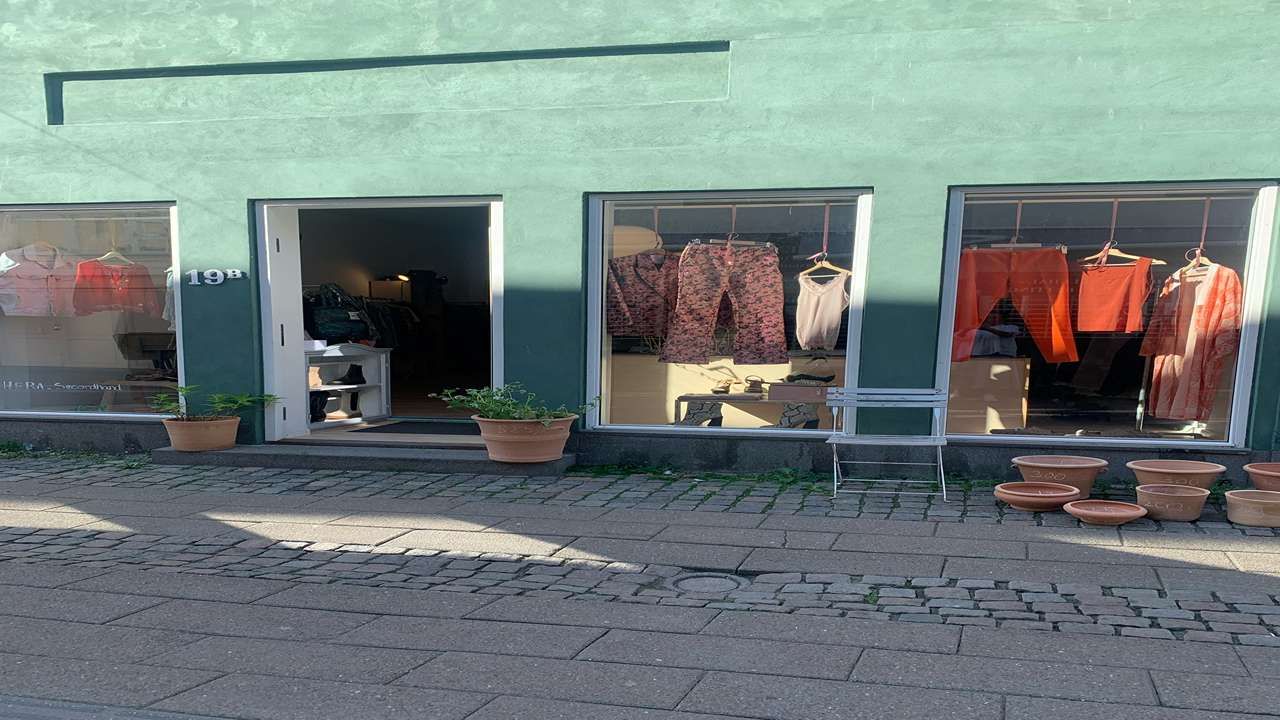 En butik med tøj og potter på gaden og et træstol i forgrunden