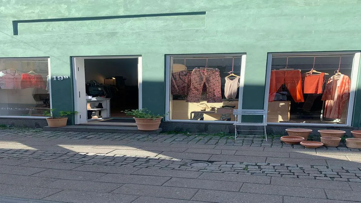 En butik med tøj og potter på gaden og et træstol i forgrunden