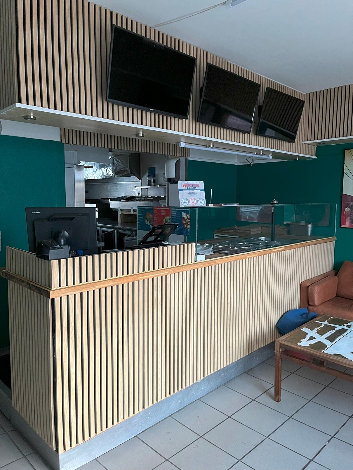 Restaurant med moderne design og tre tv-skærme bag bardisken, en computer og et legetøjskæg på et bord