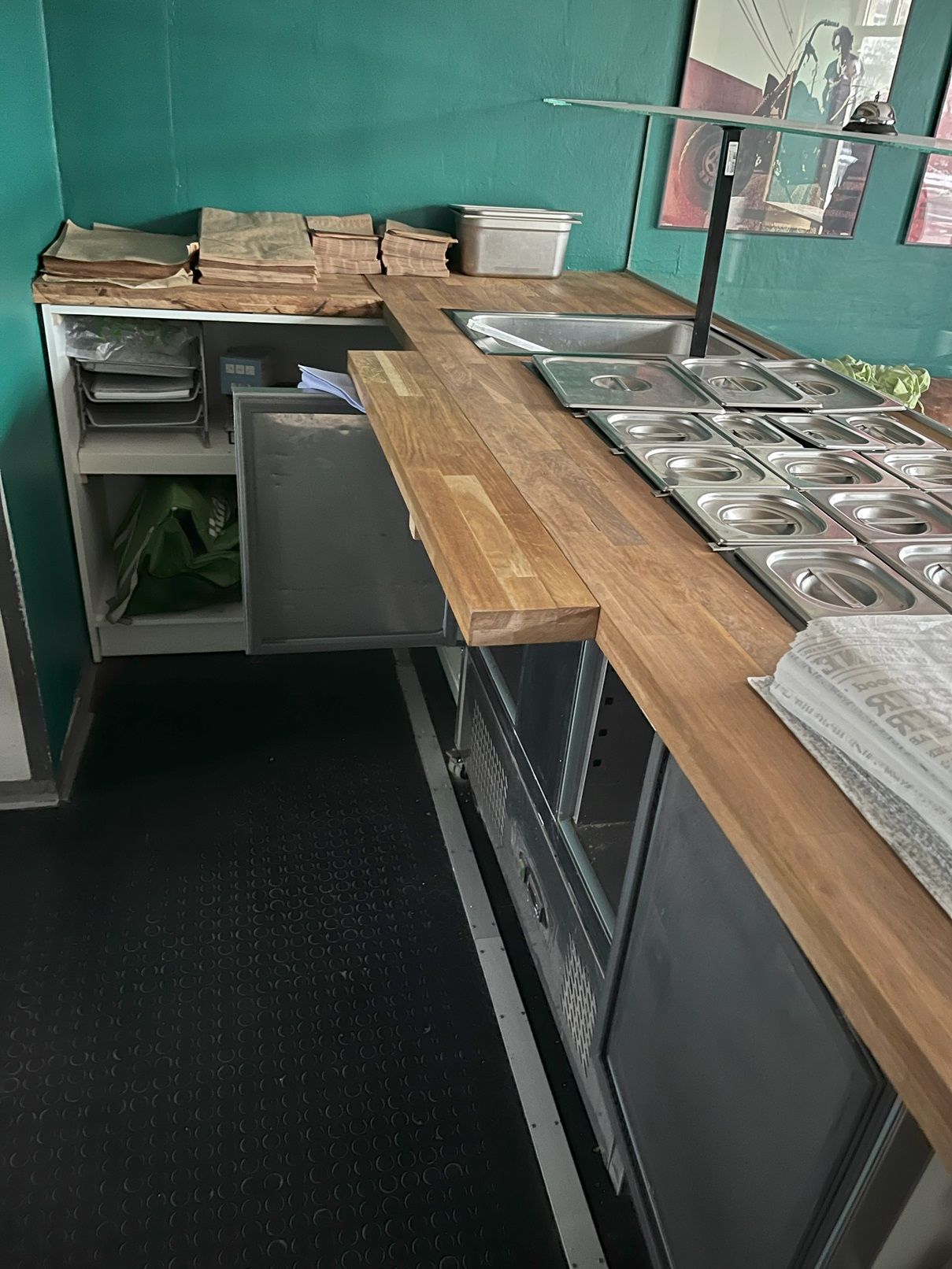 Professionelt køkken med træbenk og rustfrit stålapparater samt emballagemateriale og avis på arbejdsbordet