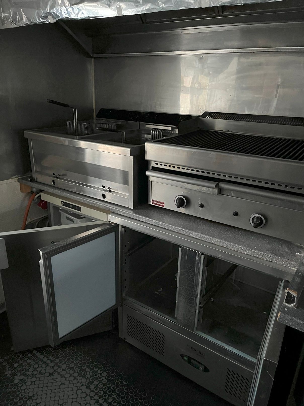 Foto af en kommerciel køkken med et frituregryde, grill og køleskab med åben dør