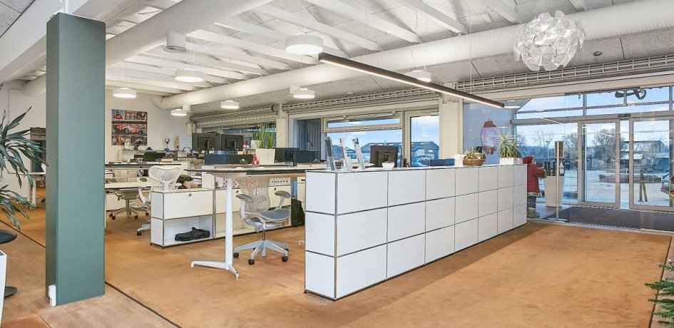 Kontorlokaler med moderne design, højt til loftet, lysekroner, skriveborde, stole, plante og udsigt til byen i Horsens