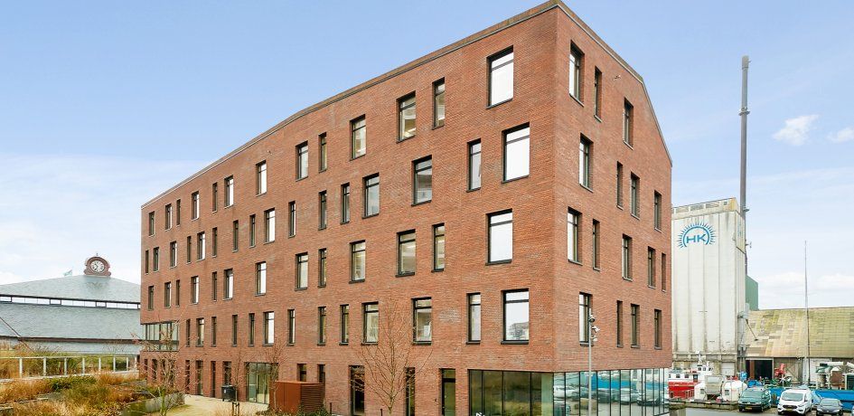 Moderne kontorejedom i røde teglsten med store ruder og glasdøre i en by. Parker og gamle bygninger i baggrunden samt biler