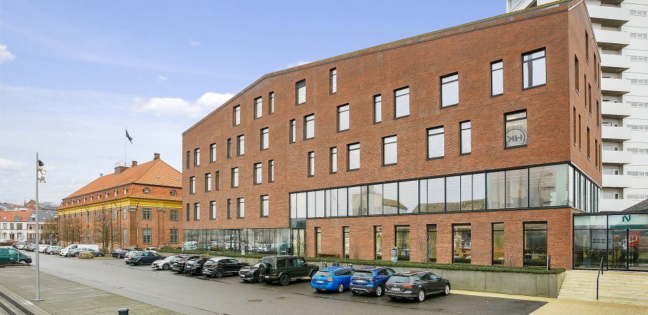 Moderne lejemål i København med en stor parkeringsplads og flere biler parkeret, og et rødt bygningsværk med flere vinduer