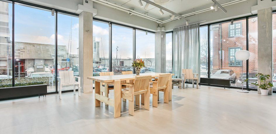 Moderne stue med massivt træbord og stole, høje ruder og lyse loftslampe og hvidt gulv